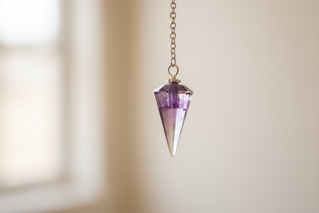 A crystal pendulum suspended from a chain, used for dowsing and intuitive guidance in crystal healing practice