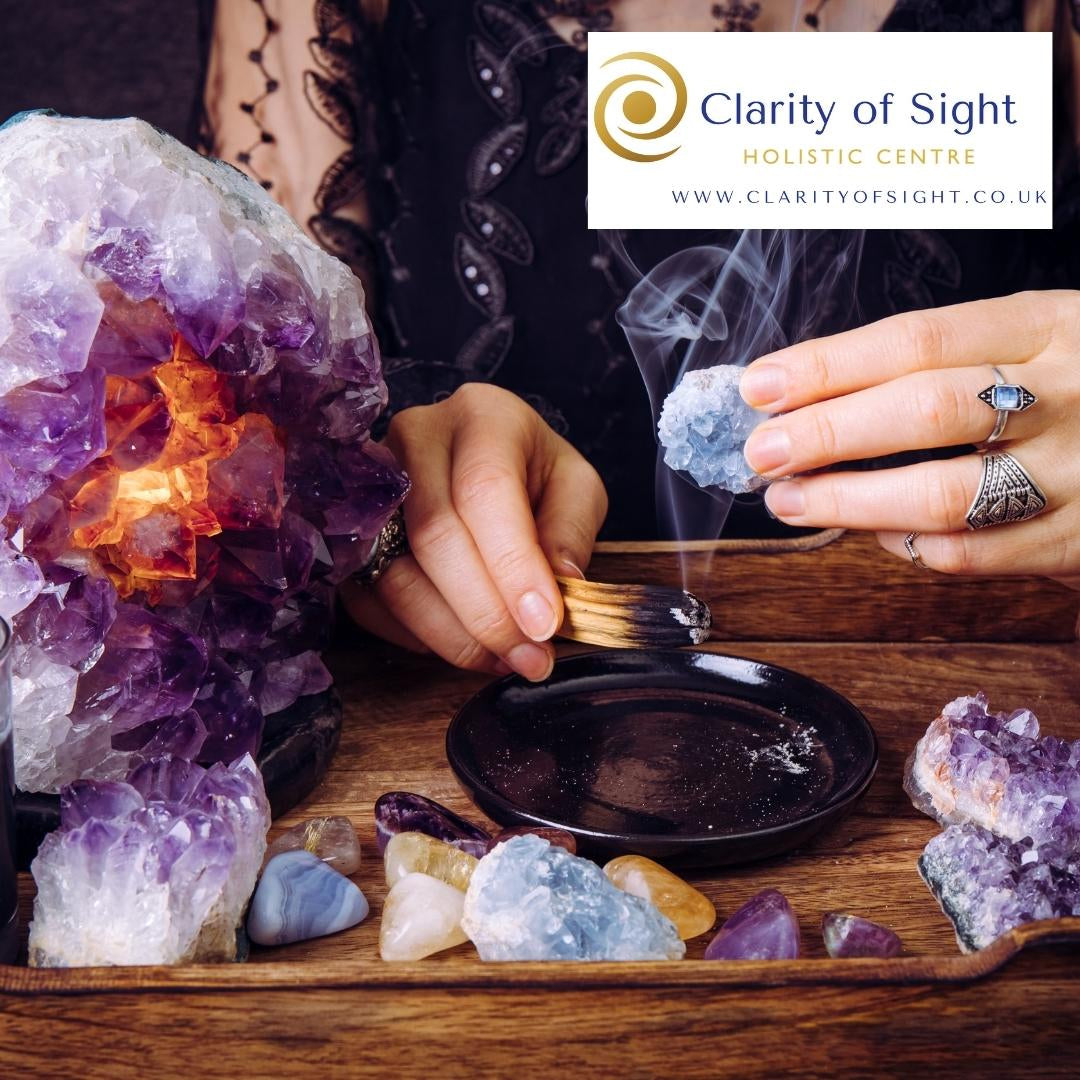 Healing crystals being cleansed with a sage smudge stick, surrounded by amethyst, rose quartz and clear quartz